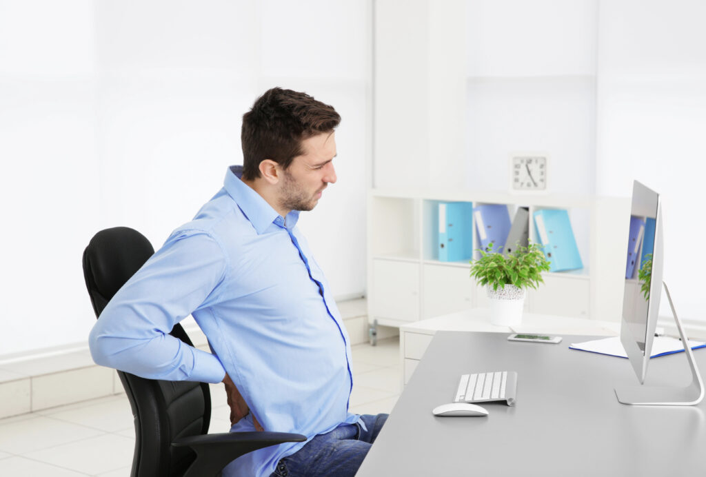 Man sitting at a desk holding his lower back in pain, needing chiropractic care for back pain relief in Libertyville Illinois